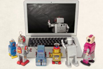 toy robots around a laptop watching a teacher robot write on the computer screen.