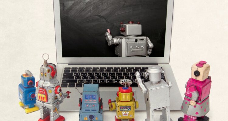 toy robots around a laptop watching a teacher robot write on the computer screen.